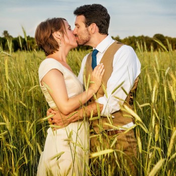 Bride and groom kiss in field