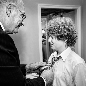 Grandfather of bride knots tie of youngest groomsman