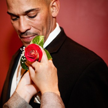 Groom in tuxedo gets pinned with red rose boutonniere