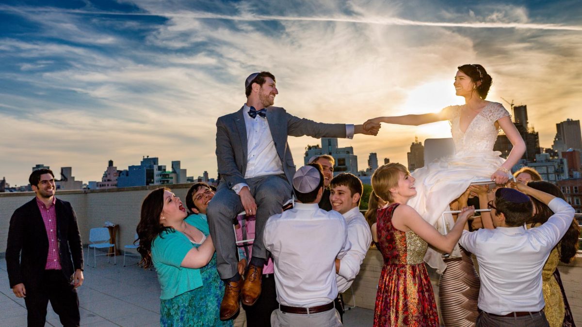 Bride and groom lifted on a chair during the hora on a rooftop