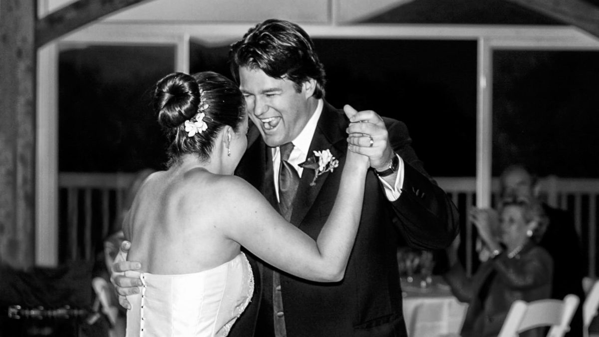 B&W photo of a bride and groom laughing and dancing