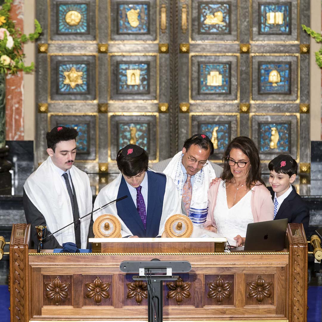 Bar mitzvah celebrant reading Torah surrounded by family